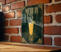 A sign with the text "MEXICAN 75" and an illustration of a glass of Mexican beer or cocktail, placed on a wooden surface against a brick wall.