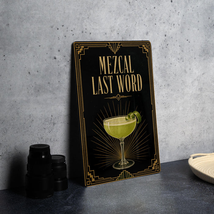 a framed poster with an illustration of a cocktail glass and the text "MEZCAL LAST WORD" on it, placed on a countertop next to some black camera lenses.