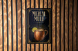 A sign for a Mezcal Mule, featuring an illustration of a copper mug with a lime slice, is displayed on a wooden wall.