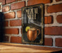 A sign for a mezcal mule, featuring an illustration of a copper mug with a lime slice, is displayed on a brick wall.