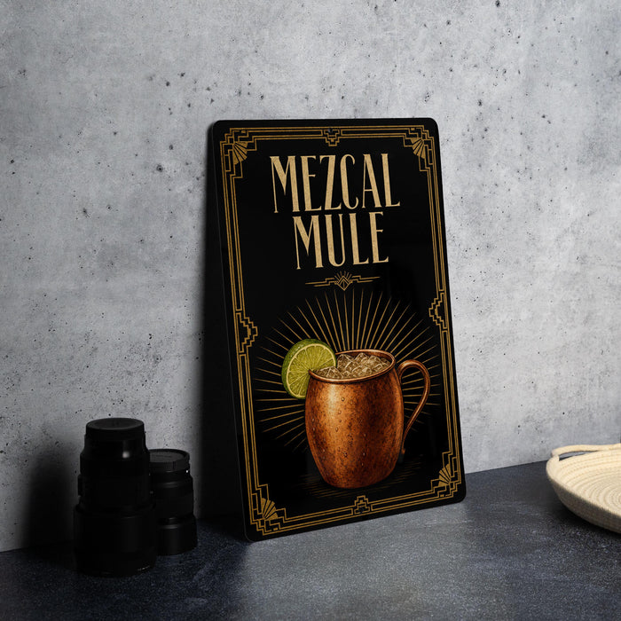 A framed poster or sign advertising a Mezcal Mule cocktail, featuring an illustration of a copper mug filled with the drink and garnished with a lime slice.
