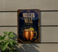 a sign for a Moscow Mule cocktail, with a copper mug containing a drink and a lemon slice, set against a dark background with decorative elements.