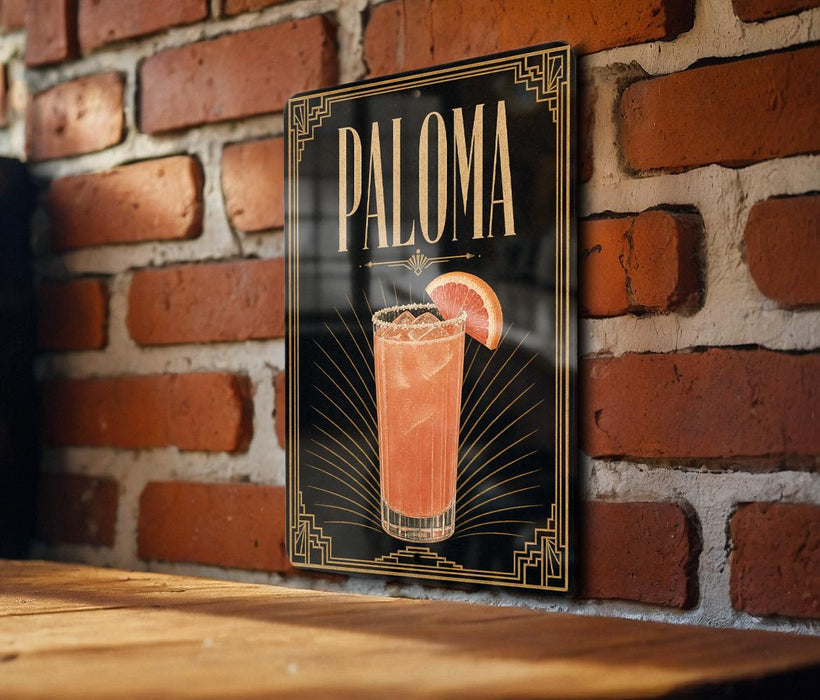 A framed poster of a cocktail called "Paloma" is displayed on a brick wall.