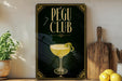 A framed poster with the text "PEGU CLUB" and an illustration of a cocktail glass on a wooden shelf.
