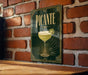 A framed poster of a cocktail called "Picante" is displayed on a brick wall, featuring a glass of the drink and a lime wedge.