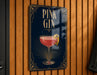 A sign with the text "PINK GIN" and an illustration of a pink gin cocktail is displayed on a wooden wall.