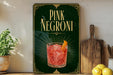 A framed advertisement for a pink Negroni cocktail, featuring an illustration of the drink and the text "PINK NEGRONI" prominently displayed.