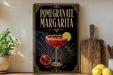 A framed poster of a pomegranate margarita is displayed on a wall, with a wooden cutting board and a potted plant to the side.
