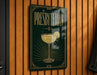 A sign for "Presbyterian" cocktail, featuring a glass of white wine with a lemon slice, is displayed on a wooden wall.