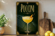 A framed poster of a yellow drink with a garnish, placed on a shelf next to a wooden cutting board and a potted plant.