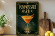 A decorative sign for a pumpkin spice martini, featuring an illustration of a martini glass with a cinnamon stick, placed on a wooden surface next to a wooden cutting board and a potted plant.