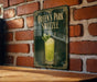 A sign for "Queen's Park Swzzle" is displayed on a brick wall, featuring an illustration of a green drink with a garnish.