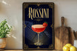 A framed poster of a cocktail called "Rossini" with a glass of the drink and a strawberry garnish, placed on a wooden shelf next to a wooden cutting board and a potted plant.