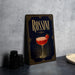 A framed poster of a cocktail called "Rossini" with a glass illustration and a strawberry garnish, placed on a gray countertop next to some black camera lenses.