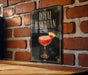 A framed poster of a Royal Hawaiian cocktail is displayed on a brick wall.