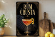 a decorative sign with the text "RUM CRUSTA" and an illustration of a cocktail glass with a lemon twist.
