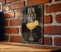 A framed poster of a cocktail called "RUM DAISY" is displayed on a brick wall, with a glass illustration of the drink and a lemon slice.