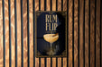 A poster with the text "RUM FLIP" and an illustration of a cocktail glass with a cinnamon stick.