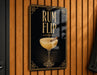 A sign with the text "RUM FLIP" and an illustration of a cocktail glass with a cinnamon stick.