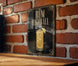 A framed poster of a rum highball cocktail is displayed on a brick wall.