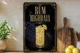 a decorative sign with the text "RUM HIGHBALL" and an illustration of a cocktail glass with a lime slice. The sign is displayed on a wooden surface, with a potted plant, a cutting board, and some lemons nearby.