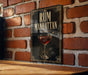 A framed poster with the title "RUM MANHATTAN" and an illustration of a glass of rum is displayed on a brick wall.
