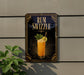 A sign for a rum swizzler cocktail is displayed on a wall, with a plant visible to the left.