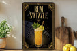 A framed advertisement for a rum swzzle cocktail, featuring an illustration of a tall glass filled with a yellow drink and garnished with a lemon slice and mint leaves.