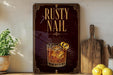 a rustic sign with the text "RUSTY NAIL" and an illustration of a glass of amber-colored liquid with a lemon twist.