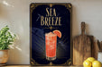 a framed advertisement for a Sea Breeze cocktail, with a glass of the drink and a slice of orange on the poster.