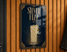 A sign for "Silver Fizz" cocktail, featuring an illustration of a tall glass filled with a yellow drink and a lemon twist.