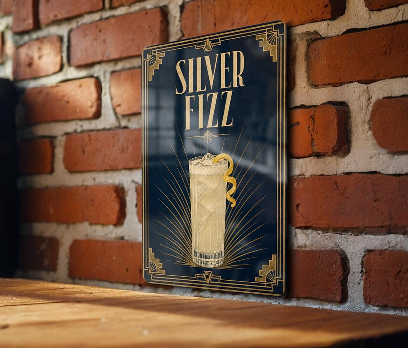 A framed poster of a cocktail with a lemon twist, displayed on a brick wall.