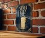 A framed poster of a cocktail with a lemon twist, displayed on a brick wall.