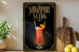 A framed poster advertising a Singapore Sling cocktail, featuring an illustration of the drink and decorative elements.