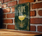 A green sign with a yellow cocktail glass on it, mounted on a brick wall.