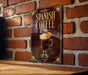 A sign for Spanish coffee is displayed on a brick wall, featuring an illustration of a coffee drink with whipped cream and an orange slice.