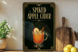 a framed advertisement for spiked apple cider, with a glass of the drink and a cinnamon stick displayed on a wooden surface.