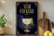 a decorative sign for a "Star Cocktail" with a glass illustration and a lemon twist, placed on a wooden surface next to a cutting board and some lemons.