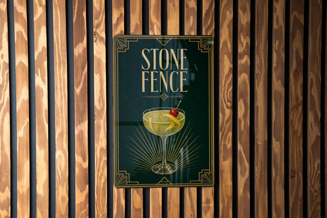 A poster for "Stone Fence" cocktail, featuring a glass of yellow liquid with a cherry garnish, is displayed on a wooden wall.