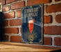 A framed poster of a strawberry champagne drink is displayed on a brick wall.