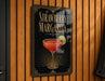 A framed poster advertising a strawberry margarita, featuring a close-up image of a strawberry margarita cocktail with a lime wedge.