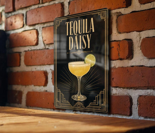 A framed poster of a tequila daisy cocktail is displayed on a brick wall, with a wooden table below it.