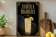 A framed advertisement for tequila highball, featuring a glass of tequila with a lime slice, is displayed on a wall next to a wooden cutting board and a potted plant.