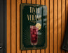 A sign for "Tinto de Verano" with a glass of red drink and a lemon slice, displayed on a wooden wall.