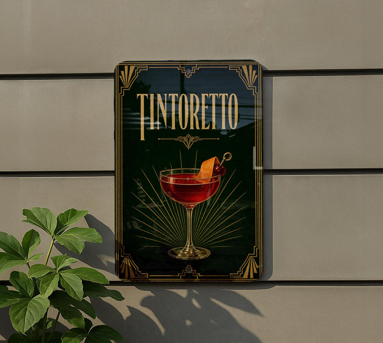 A framed poster of a Tintoretto cocktail is displayed on a wall, with a plant visible to the left.
