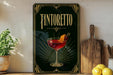 a framed poster of a glass of Tintoretto cocktail, with a wooden cutting board and a potted plant in the background.