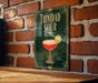 A framed poster of a cocktail called "Trinidad Sour" is displayed on a brick wall.