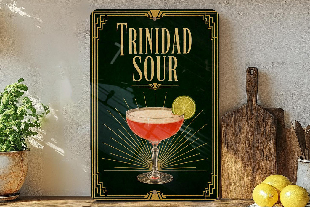 A framed poster of a cocktail called "Trinidad Sour" is displayed on a wall, with a wooden cutting board and a potted plant to the side.