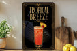 A framed poster advertising a tropical breeze cocktail, featuring a glass of the drink with a pineapple and a cherry on the rim.