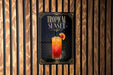 A sign for a tropical sunset cocktail is displayed on a wooden wall.